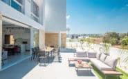 Modern outdoor patio area with dining table, lounge sofa, and potted plants under clear sky in Protaras Holiday Rentals.