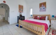 Cyprus Villa Rent Serenely decorated white bedroom with wooden bed, red accents, and symmetrical artwork.