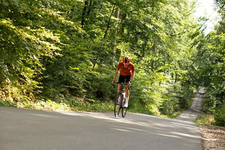 Cyclist in red jersey riding uphill on sunny forest road in Cyprus.