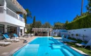 Luxurious poolside setting with modern villa in Paphos, loungers, and lush green garden.