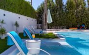 Luxurious poolside villa in Paphos Cyprus  with modern loungers, greenery, and refreshing drink on a sunny day.