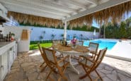 A stylish outdoor dining area with a pool, pergola, and lush greenery.