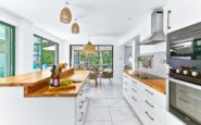 Modern, stylish kitchen with white cabinetry, wooden island, and garden view through large windows.