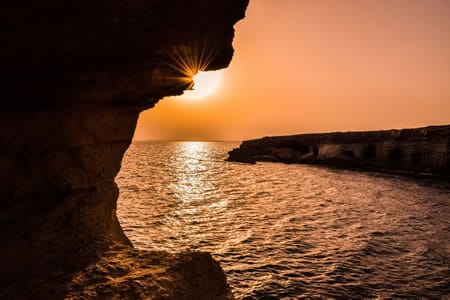 Captivating sunset over rocky coastal scene in Polis Chrysochous, reflecting golden hues on water.